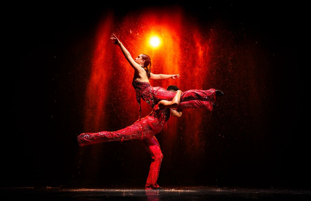 Danseur sous la pluie dans le studio, éclairage dramatique créant des reflets sur le sol mouillé