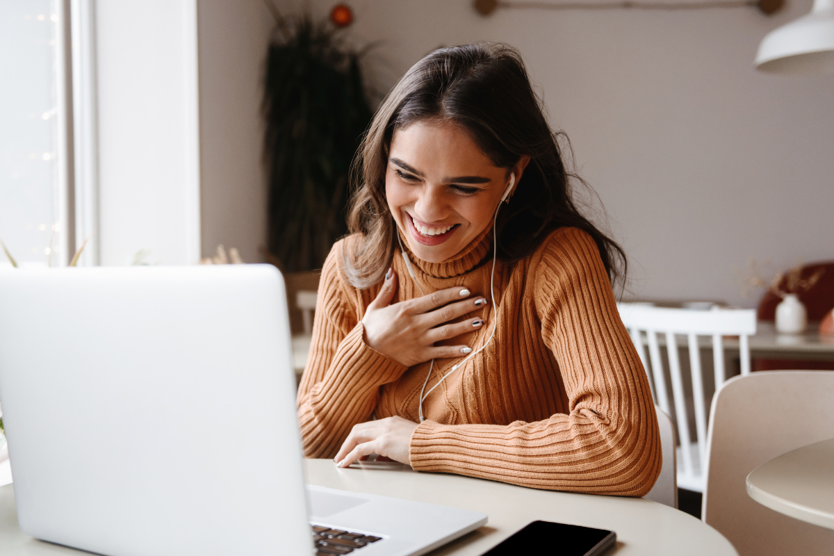 Femme souriante en appel vidéo professionnel avec ses clients, dans un bureau à domicile bien aménagé